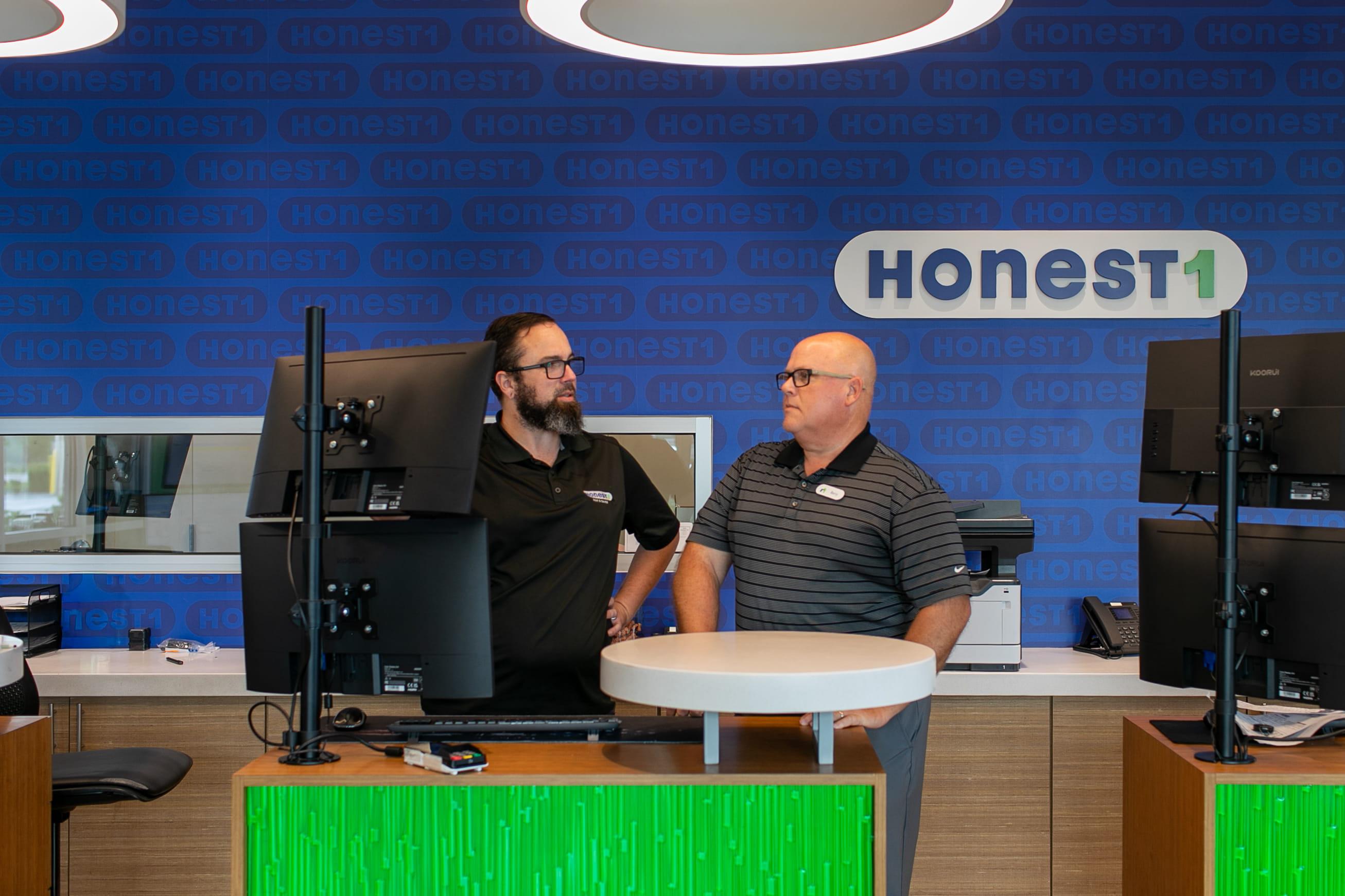An Honest1 Auto Care franchisee and manager talking inside their auto repair shop reception area.